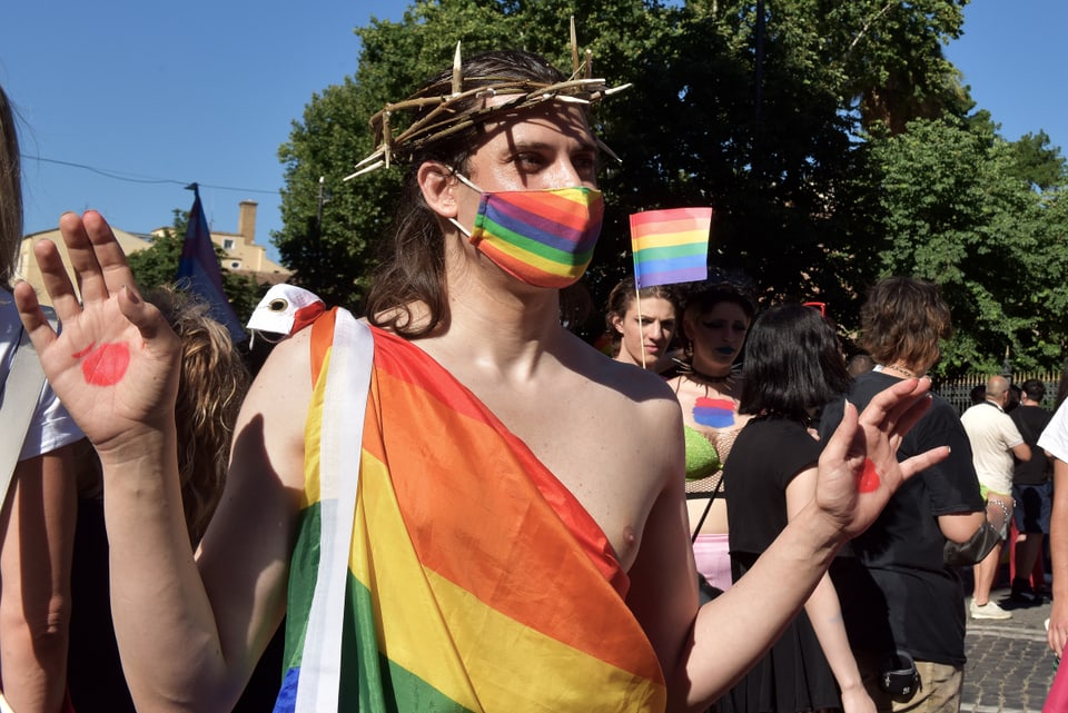 A young man holding a wooden crown of thorns and a rainbow flag