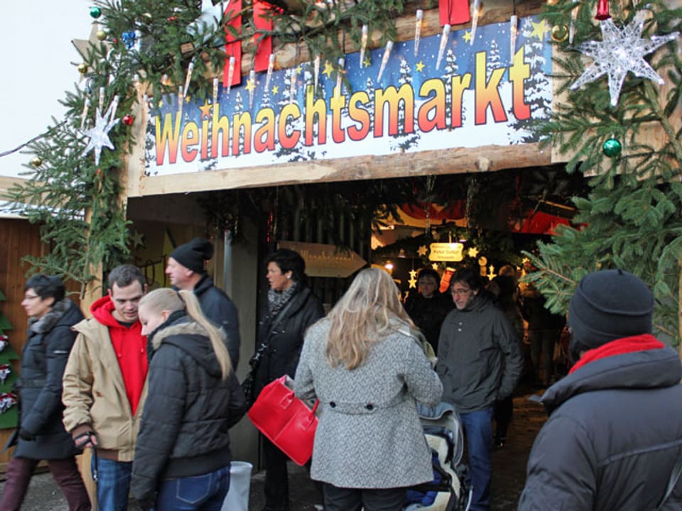 Leute stehen vor einem Eingang, beschriftet mit Weihnachtsmarkt