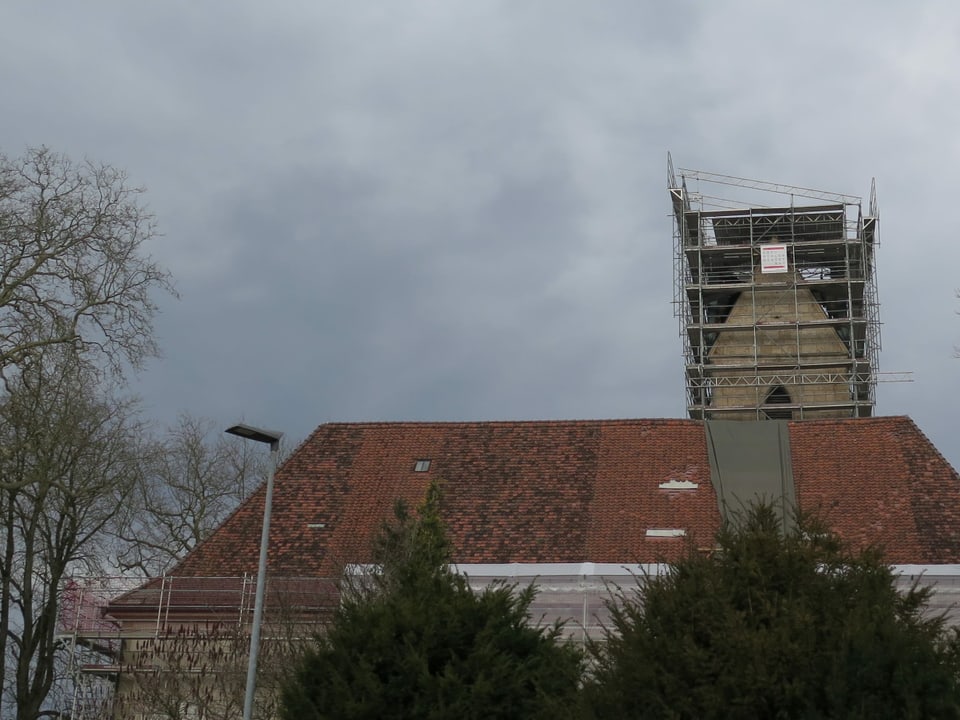 Kirchturm im Gerüst, hinter einem grossen Hausdach.