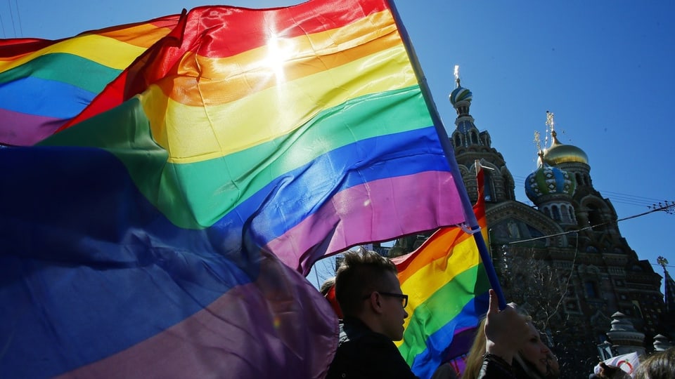 Menschen halten eine Regenbogenflagge in Russland in die Höhe.