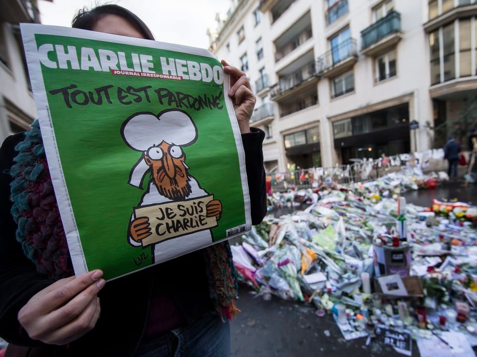 Eine Person hält das Titelbild von «Charlie Hebdo»