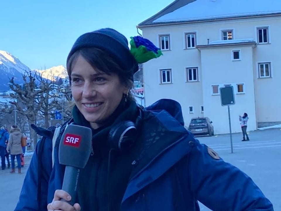 Dania hält lächelnd ein Mikrofon in der Hand. An ihrer blauen Mütze steckt eine grün-blaue Papierblume.