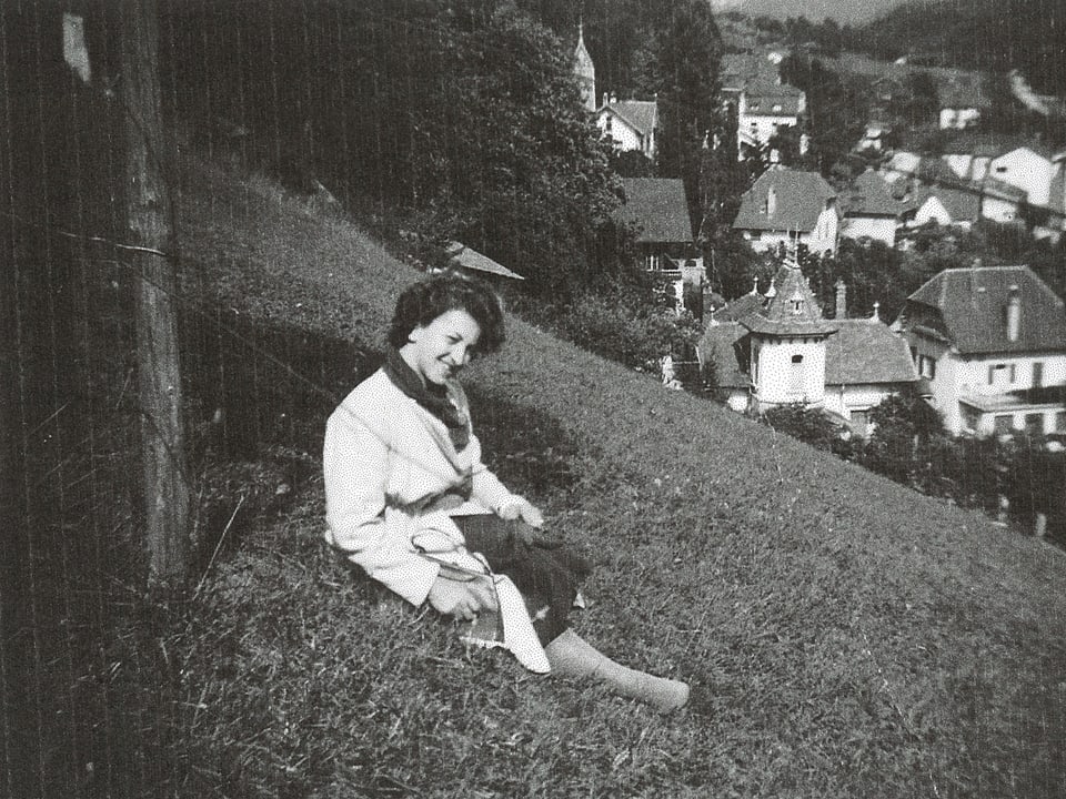 Die junge Frau sitzt auf einer Wiese oberhalb eines Dorfes.