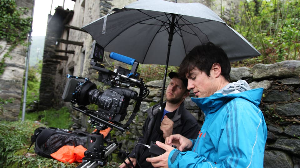 Zwei Männer schützen sich und ihre Kameraausrüstung mit einem Regenschirm