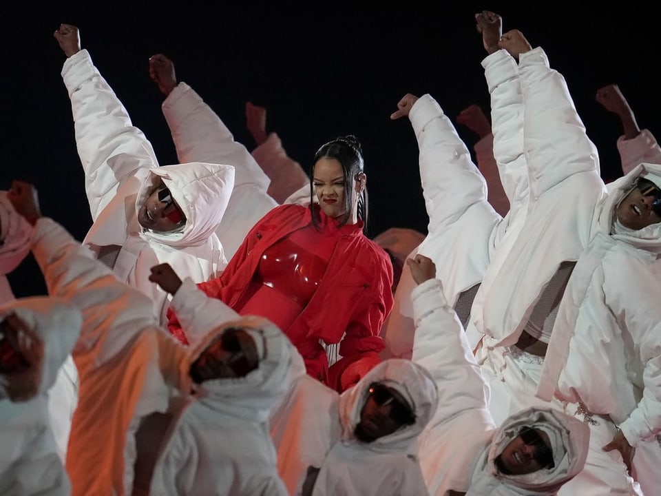 Rihanna in rot umgeben von Tänzern in weiss.