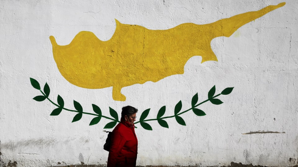 Frau spaziert vor einer Fassade durch, auf der die zypriotische Flagge abgebildet ist