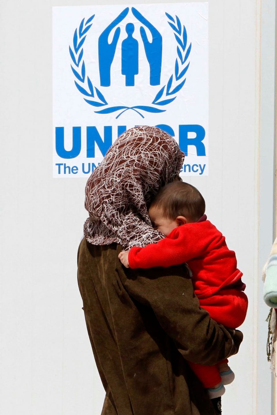 Eine Frau trägt ein Kleinkind und sieht sich ein Logo von UNHCR an.