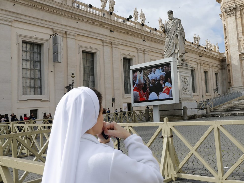 Eine Nonne betend und auf einen TV-Bildschirm schauend auf dem Petersplatz.