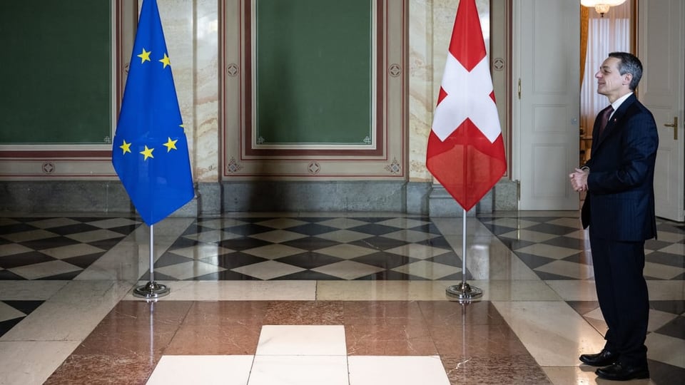 Auf einem Flur stehen die Flagge der EU und der Schweiz. Bundesrat Ignazio Cassis steht neben der Schweizer Flagge.