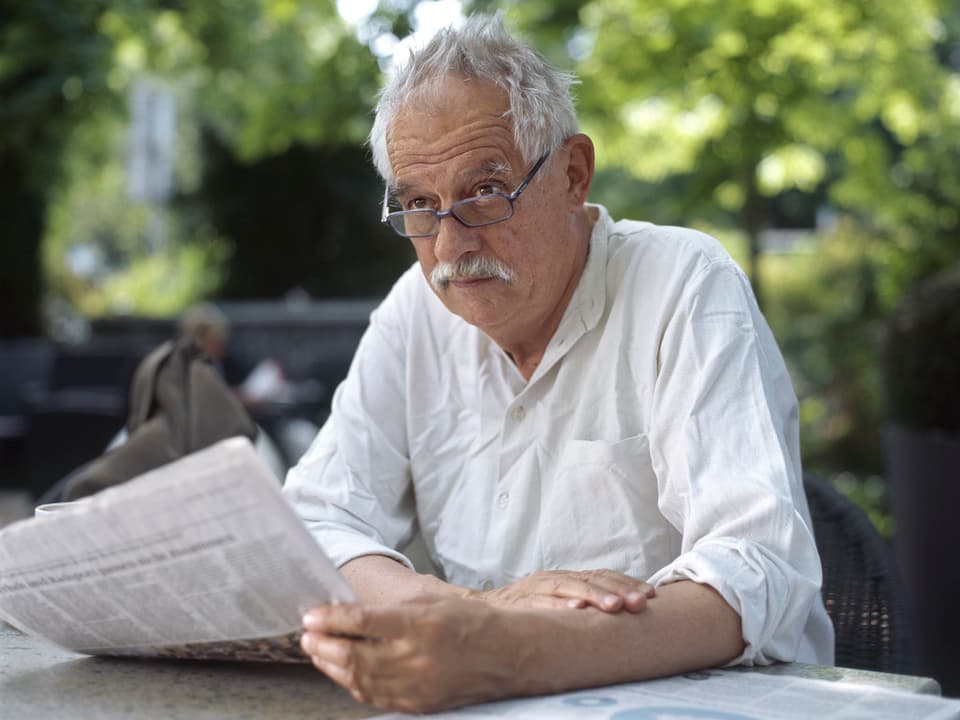 Hansjörg Schneider sitzt an einem Tisch in einem Garetn und liest Zeitung.