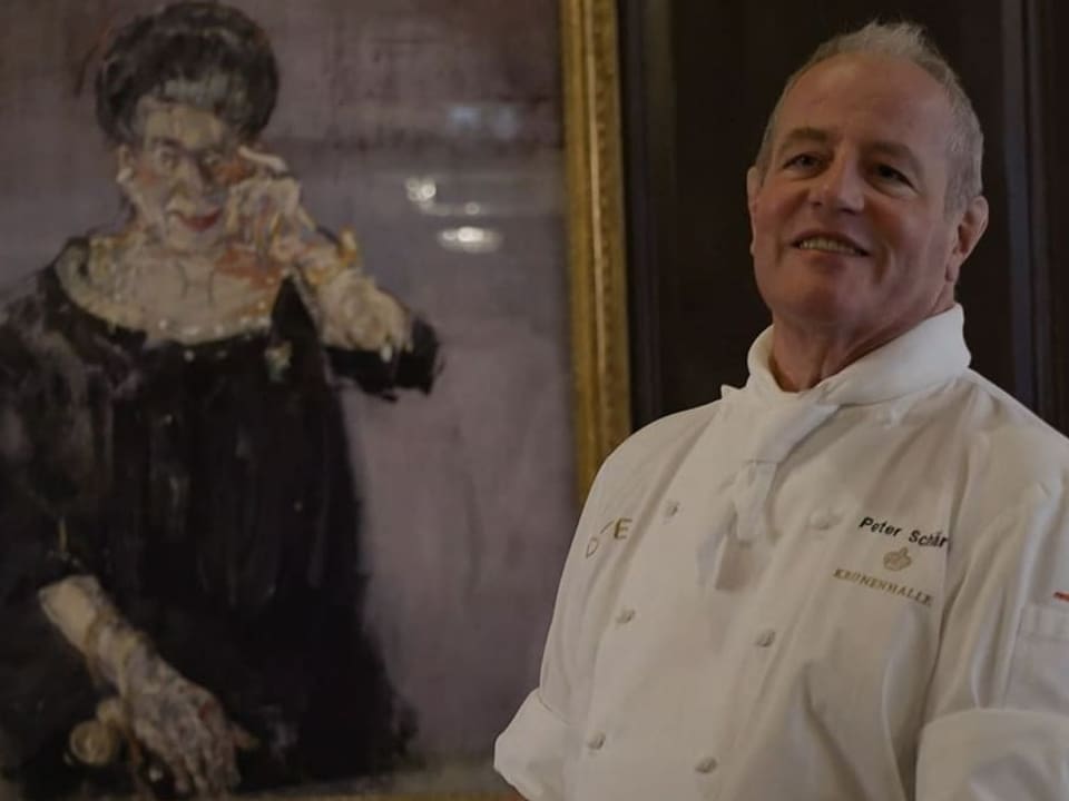 Koch in weisser Uniform steht neben einem Gemälde einer Frau.