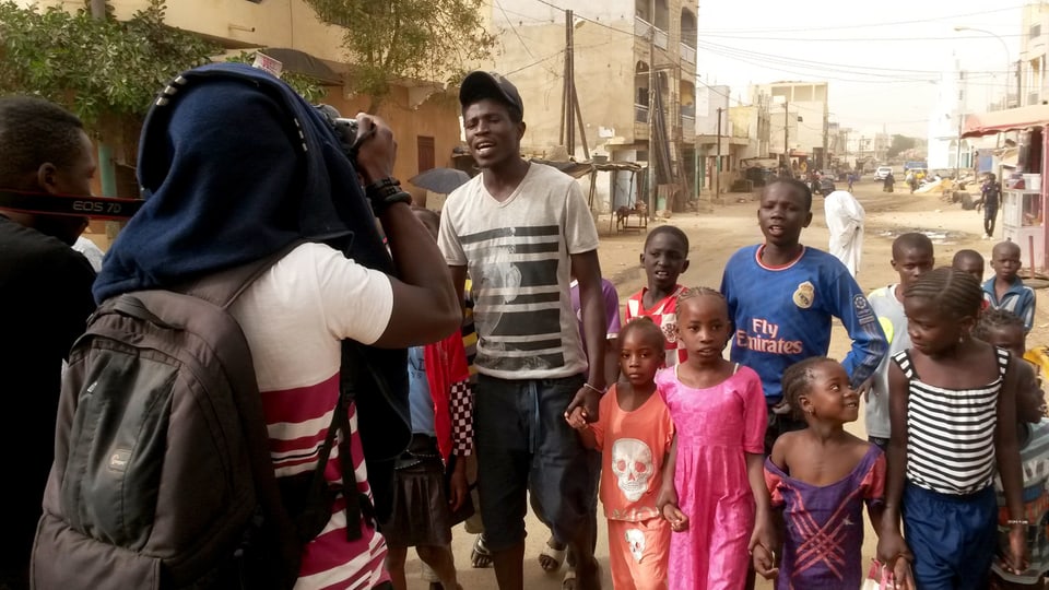 Ein Mann rappt, begleitet von einer Gruppe Kinder, und wird dabei von einem anderen gefilmt.
