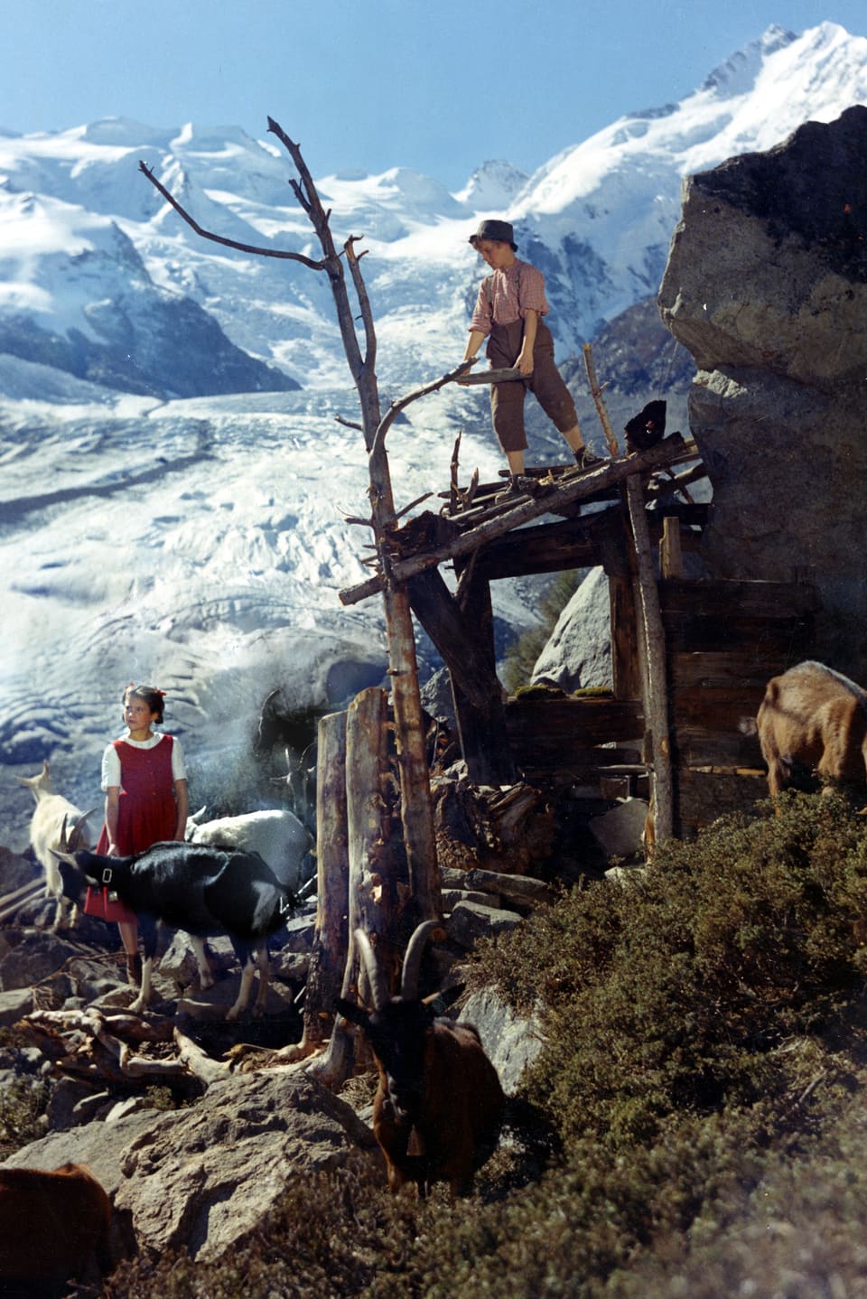 Heidi und Peter mit den Ziegen auf der Alp. Hinter ihnen erstreckt sich der Gletscher.