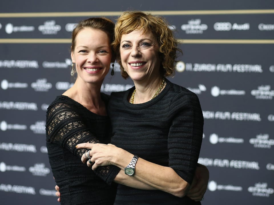 Mona Petri und Sabine Boss Arm in Arm vor einer Fotowall. 
