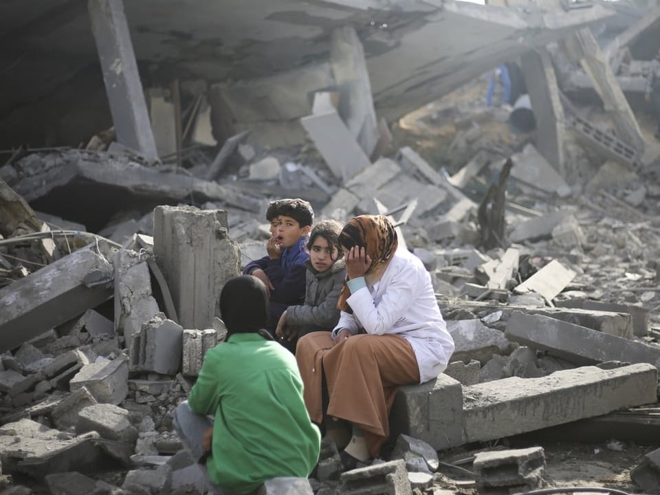 Eine Frau und drei Kinder sitzen in den Trümmern in Rafah.