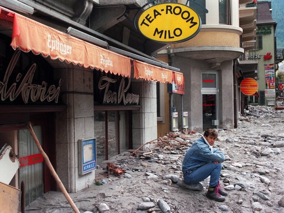 Ein Mann sitzt vor seinem zerstörten Geschäft auf einem Geröllhaufen.