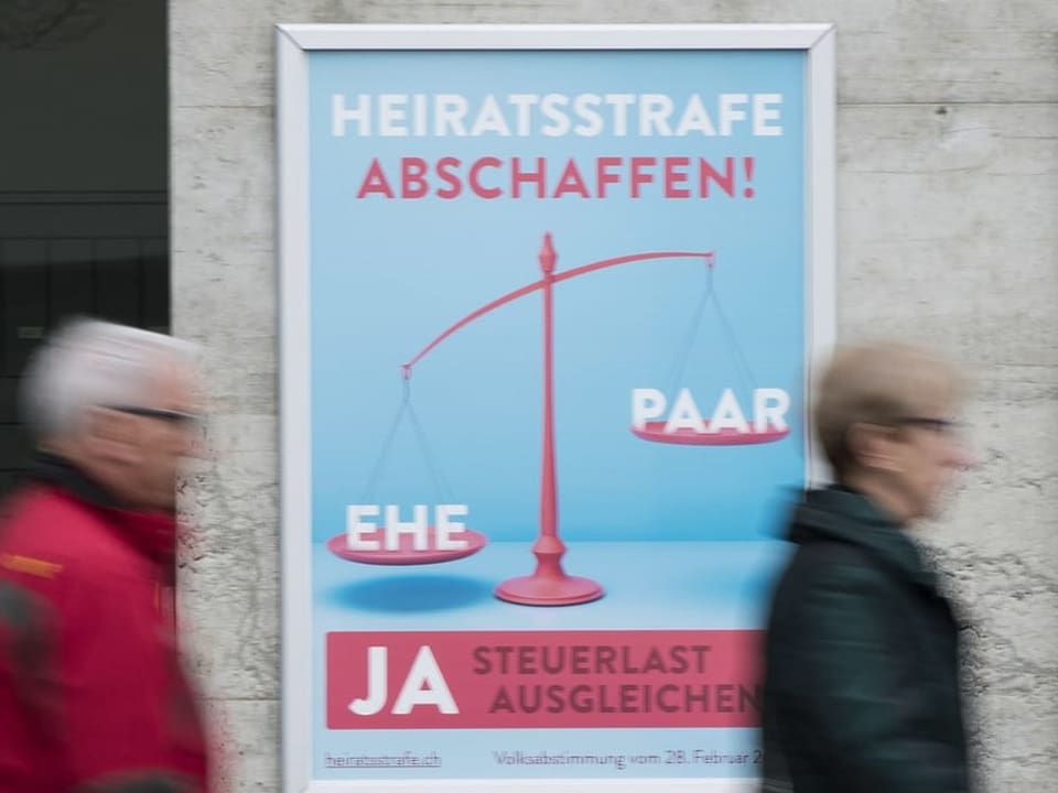 Ein Abstimmungsplakat für die Abschaffung der Heiratsstrafe hängt an der Wand, davor laufen zwei Menschen durchs Bild.