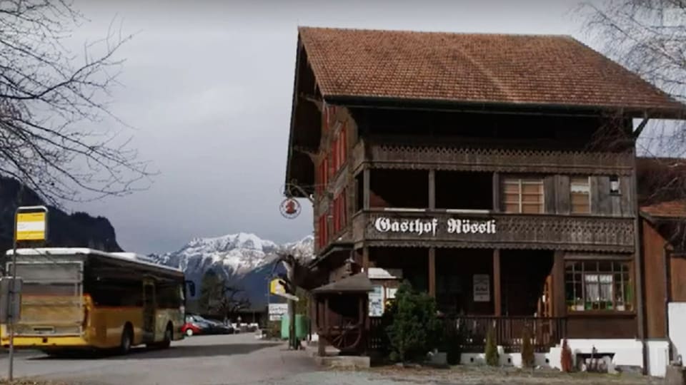 Ländliches Gebiet, links Postauto, rechts Holzhaus mit Aufschrift «Gasthof Rössli»