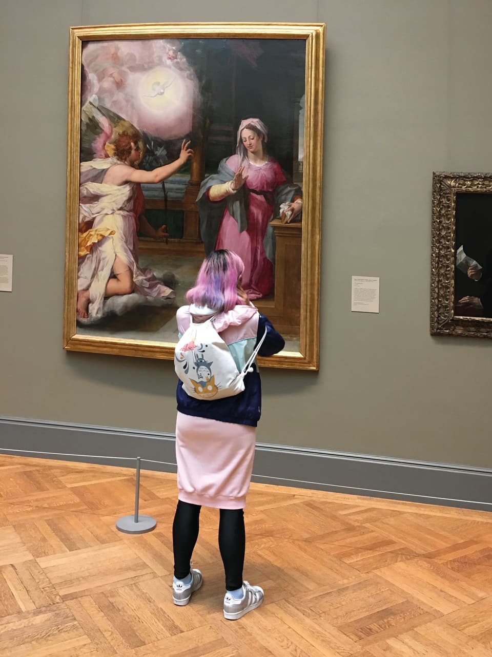 Junge Frau mit pinkem Rock und pinken Haaren steht vor einem grossen Gemälde im Museum