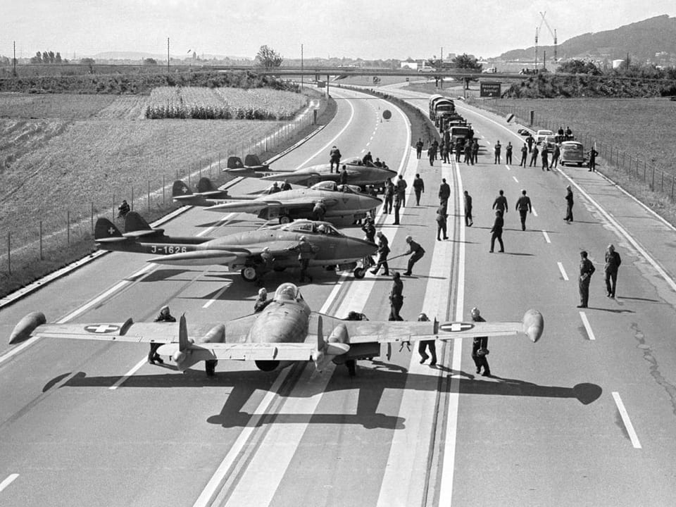 Mehrere Kampfjets stehen auf einer Autobahn; umringt von Menschen