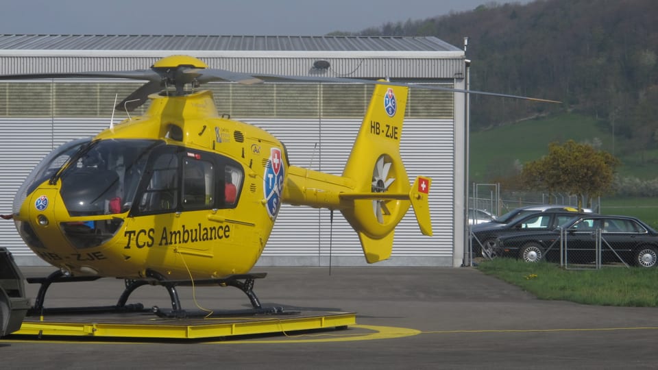 Gelber TCS Helikopter vor einem Hangar im Birrfeld. 
