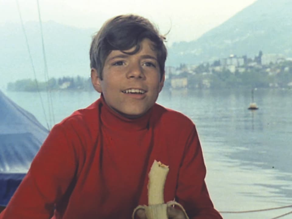 Ein Junge in rotem Pullover am Ufer eines Sees