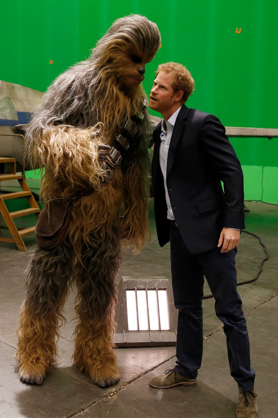 Ein Schauspieler im Chewbacca Kostüm flüsstert Prinz Harry etwas ins Ohr.