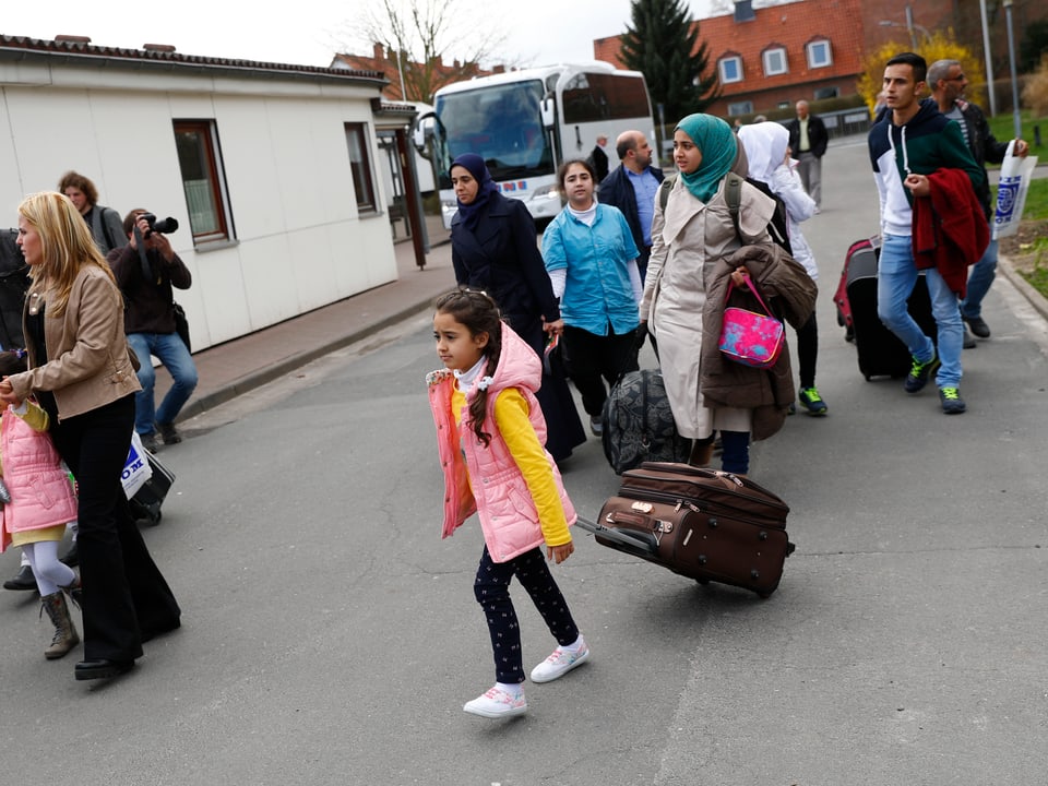 Flüchtlinge die aus einem Bus steigen und in ein Flüchtlingslager laufen. 