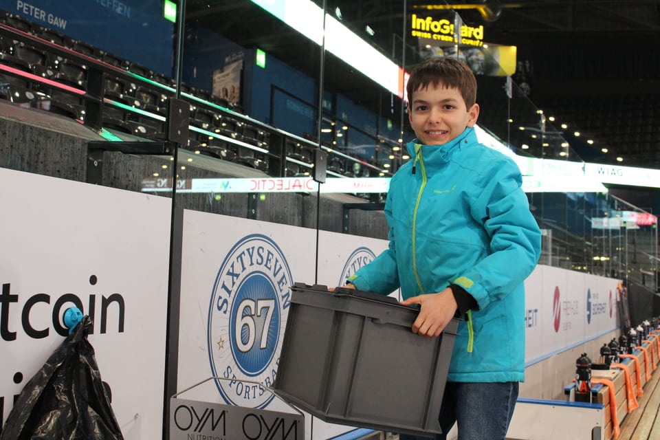 Ein Junge trägt eine Kiste, im Hintergrund stehen Flaschen.