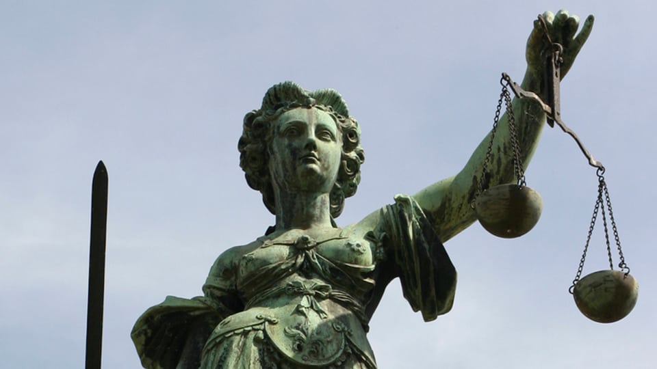 Statue der Justitia von unten fotografiert, im Hintergrund Himmel. Justita mit der Waage in der einen und einem Schwert in der anderen Hand.