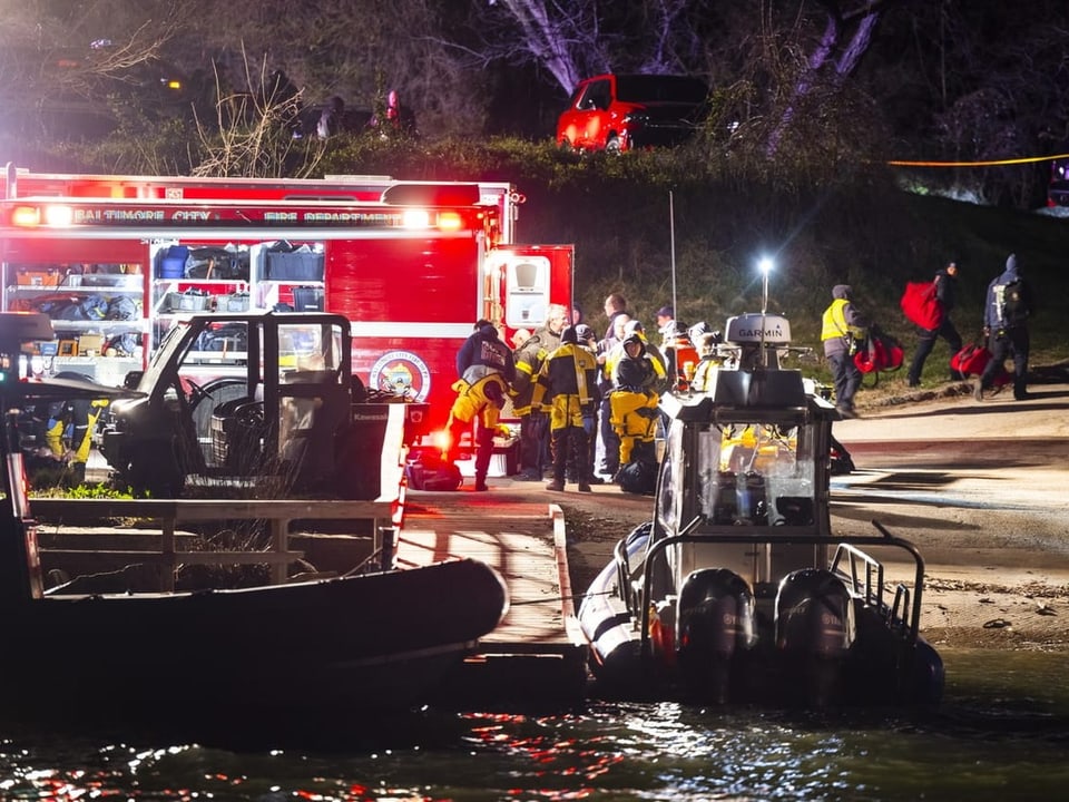 Foto in der Nacht, vorne Wasser und Boote, hinten Rettungsfahrzeuge und Personen in Feuerwehrmontur