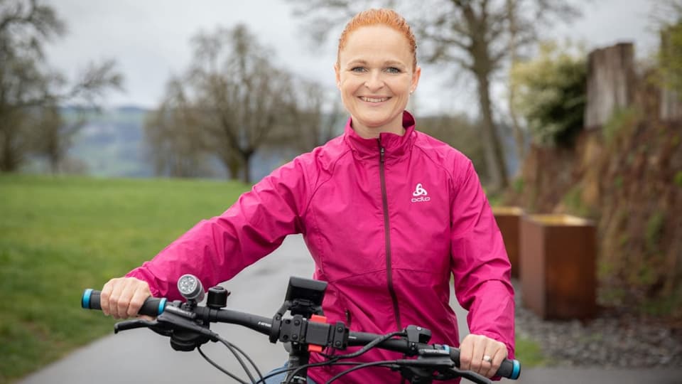 Frau mit einer pinken Jacke steht neben einem Mountain-Bike.