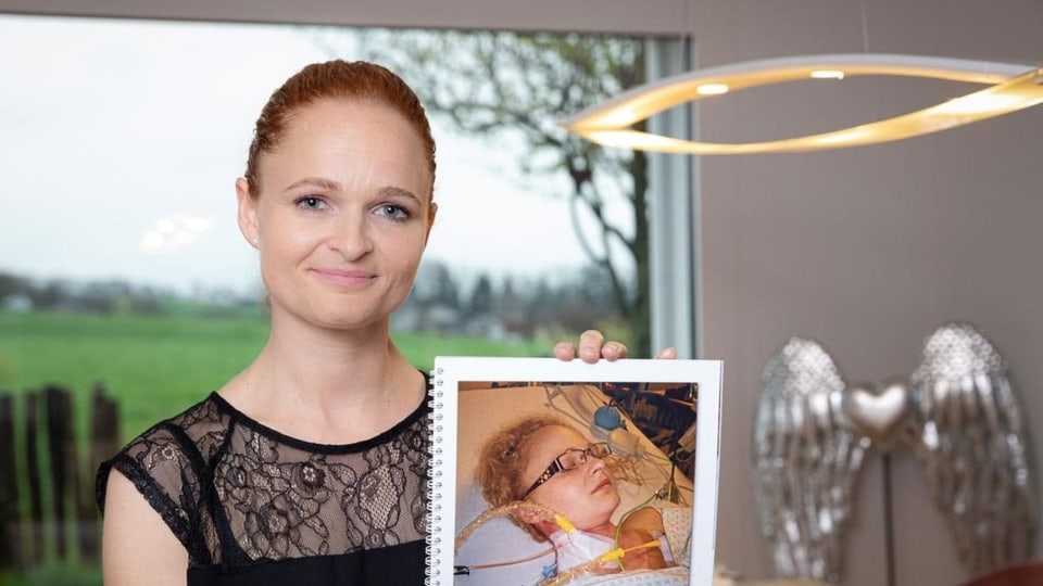 Eine Frau mit roten Haaren hält ein Foto von sich auf der Intensivstation in den Händen.
