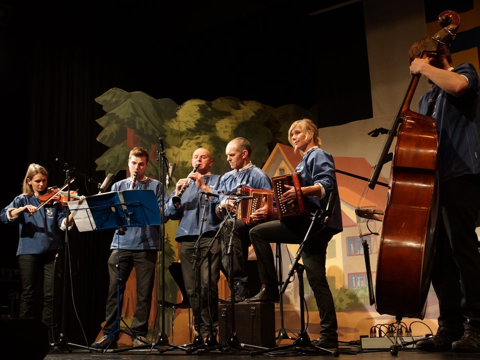 Musikantinnen und Musikanten in blauen Hemden musizieren mit Geige, Klarinette, Schwyzerörgeli und Kontrabass.