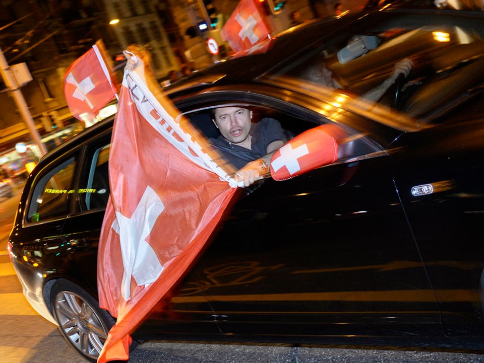 Ein Fan hält die Schweizer Fahne zu einem fahrenden Auto heraus. 