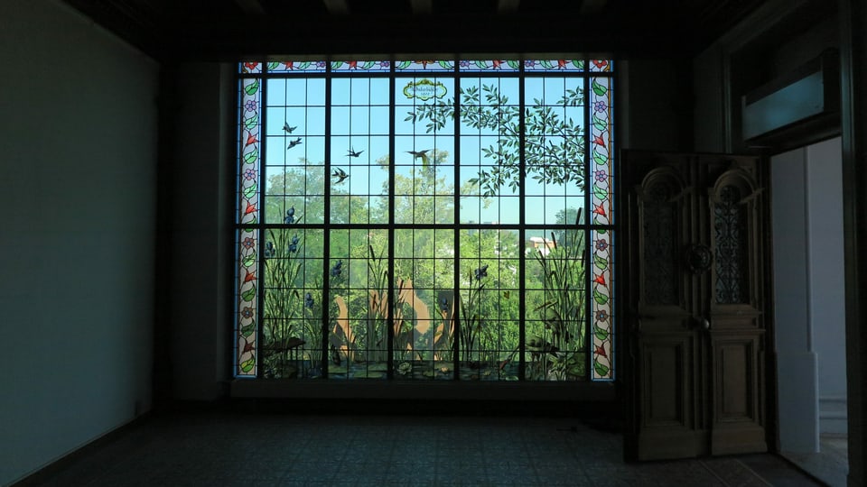 Fenster mit Malereien, daneben führt schwere Holztüre ins Freie