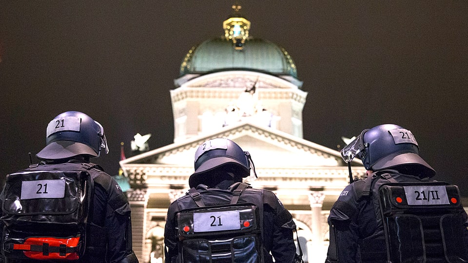 Einsatzbeamte in Kampfmontur stehen auf dieser Nachtaufnahme mit dem Rücken zur Kamera vor dem Bundeshaus in Bern.