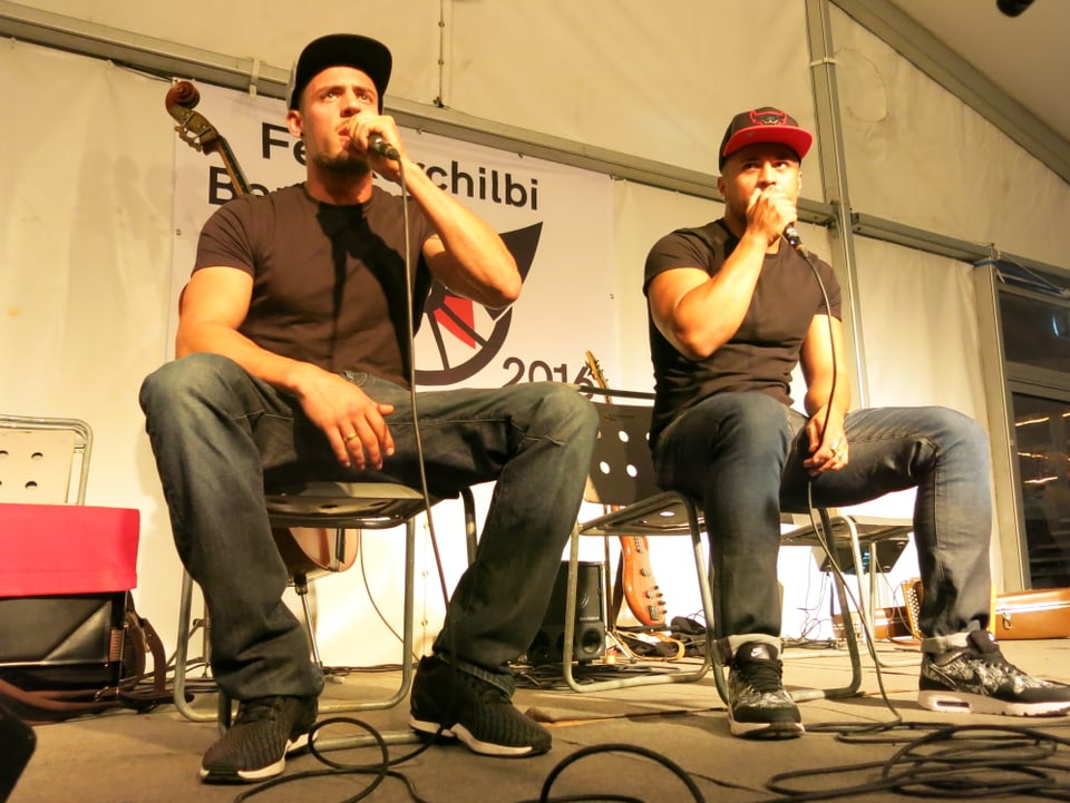 Zwei Rapper sitzen auf einer Bühne.