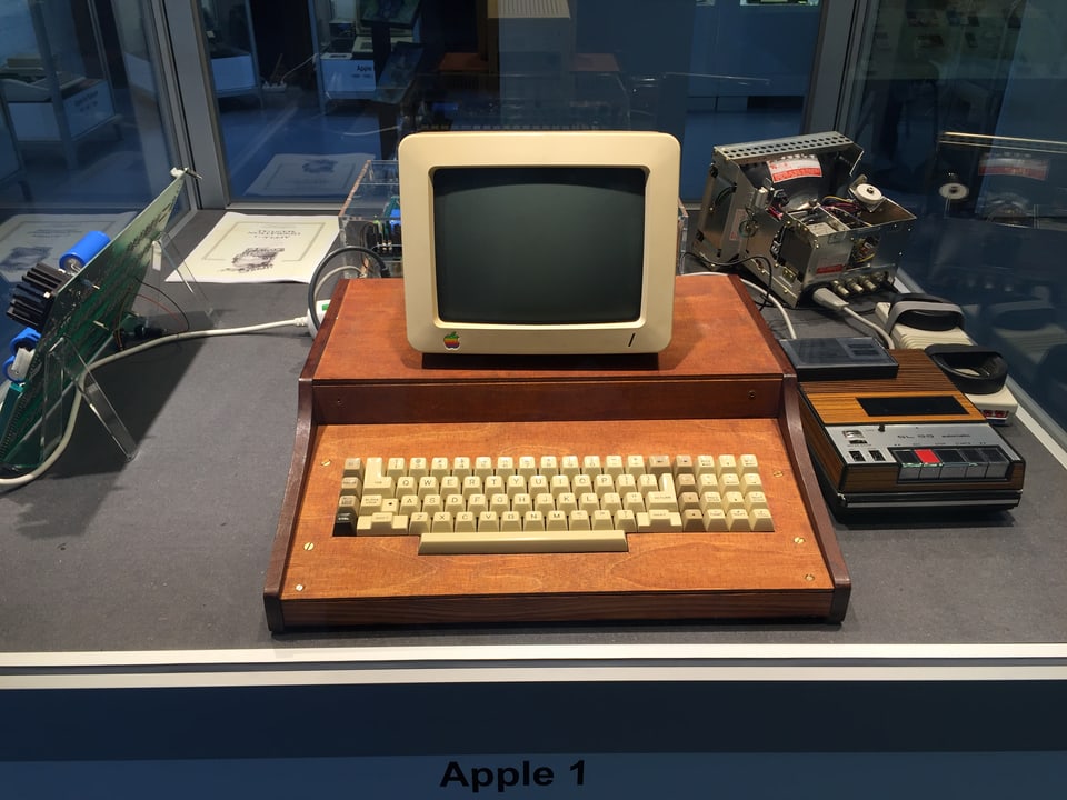 Alter Computerbildschirm auf Holzgestellt, darunter Tastatur, rechts daneben ein Kassettengerät