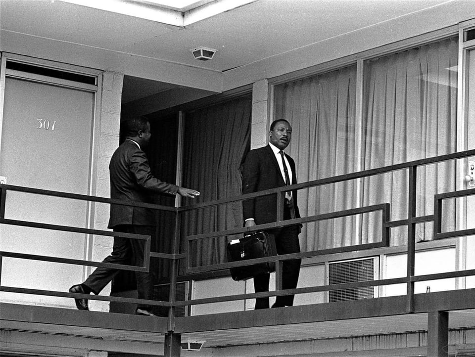 Zwei Männer in Anzügen laufen über einen Motel-Balkon