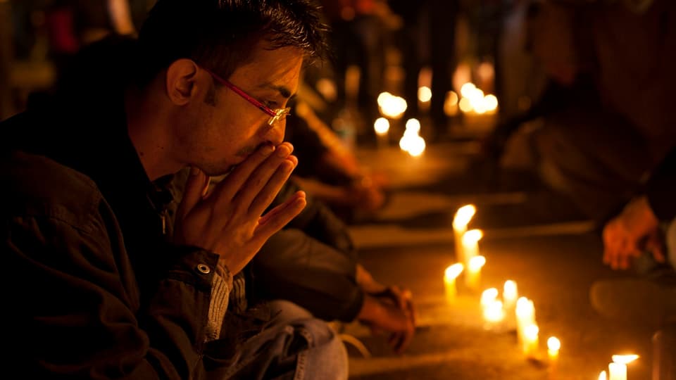 Mehrere Personen beten vor auf dem Boden stehenden Kerzen