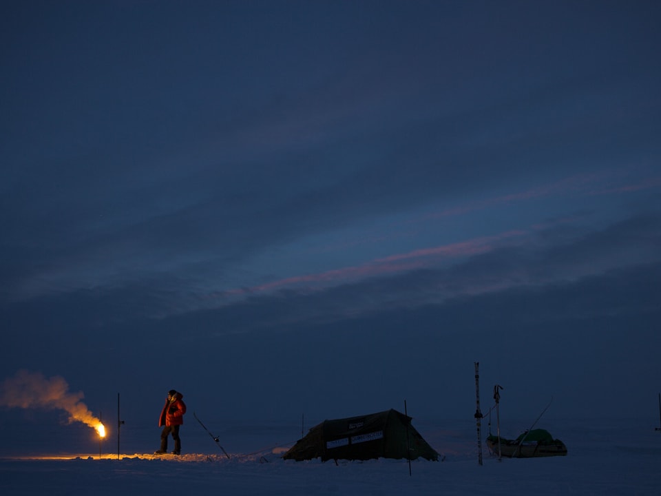 Mann in der Arktis in der Nacht mit Zaun um Zelt