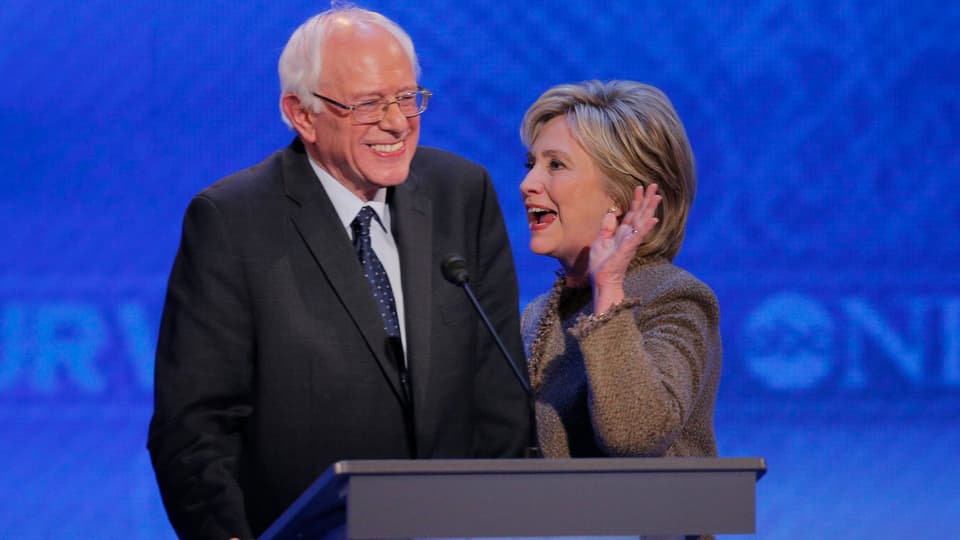 Mann und Frau stehen während TV-Debatte lachend nebeneinander, sie hebt die Hand. 