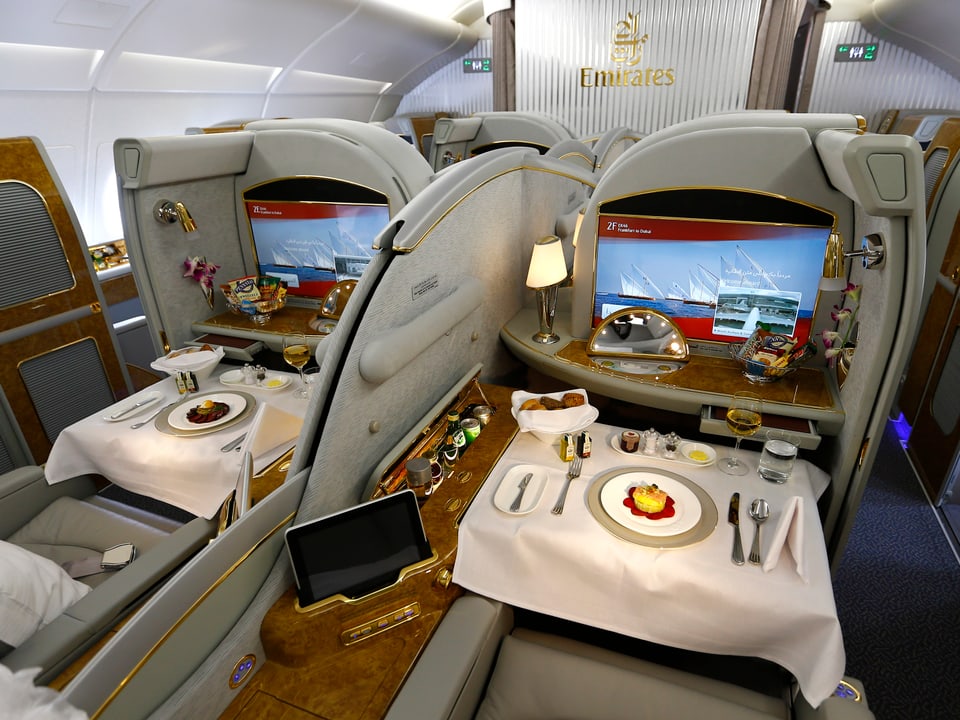 Zwei Passagier-Bereiche in der 1. Klasse, der Tisch ist gedeckt, die Bildschirme sind bedeutend grösser als in der Economy-Klasse.