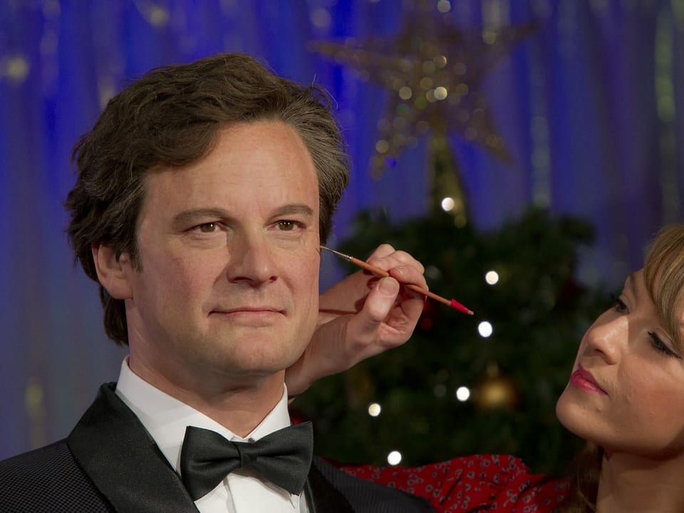 Eine Wachsfigur von Colin Firth wird von einer Frau mit einem feinen Pinsel bemalt. 