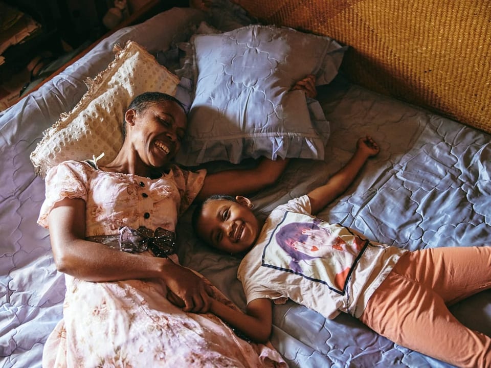 Lächelnde Frau und Mädchen liegend auf einem Bett, Hand in Hand.