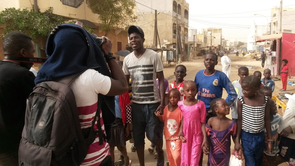 Ein Videodreh mit schwarzen Kinder in einer staubigen Strasse Dakars,