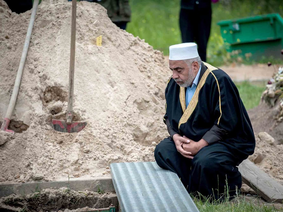 Mann kniet vor einem Grab. 
