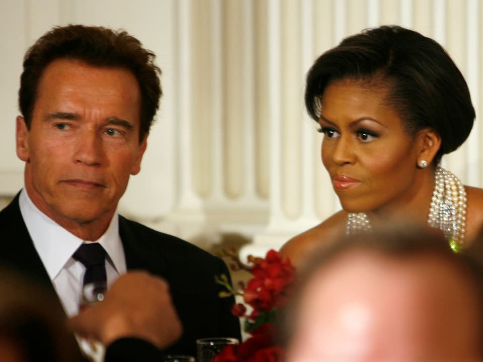 Arnold Schwarzenegger (links) sitzt neben Michelle Obama (rechts)