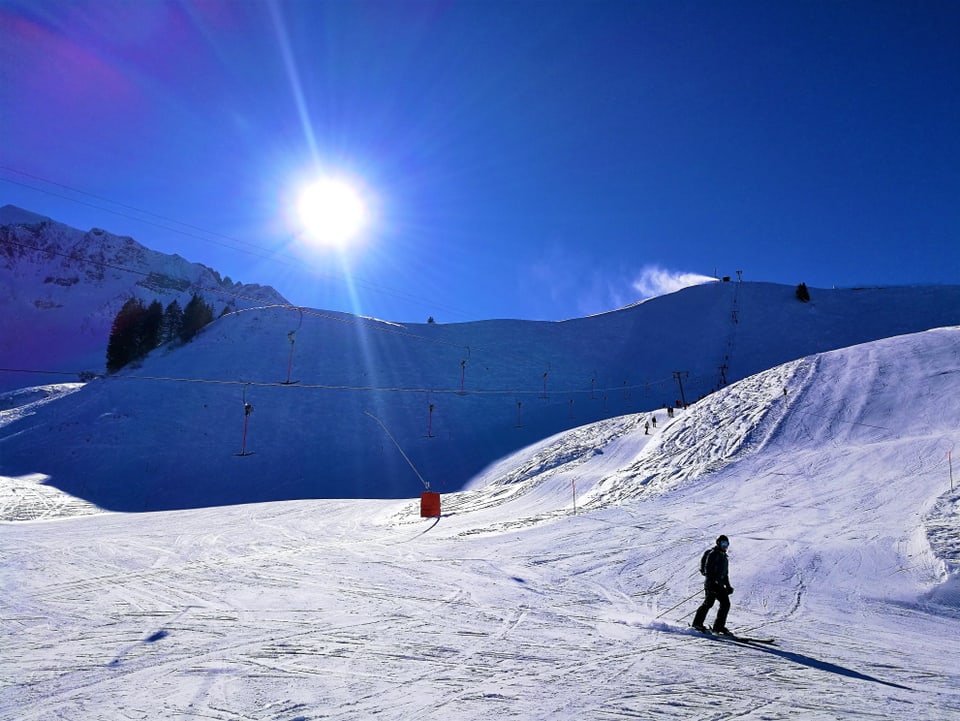 Ein Skifahrer schwingt über die glatte Pisten, die Sonne strahlt vom blauen Himmel
